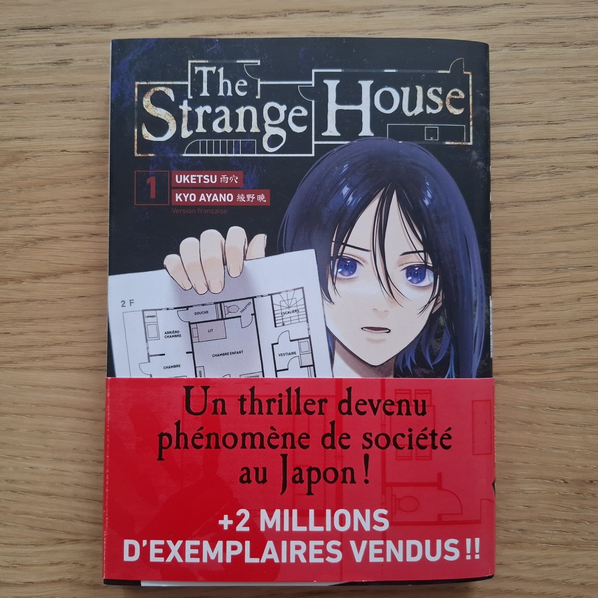 Le tome 1 du manga The Strange House - Uketsu posé sur une table, couleurs dark à dominance de noir, rouge et blanc